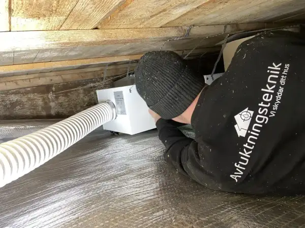 Installering av ventilation i friggebod. En tekniker arbetar med en vit ventilationsenhet under träbjälkar.