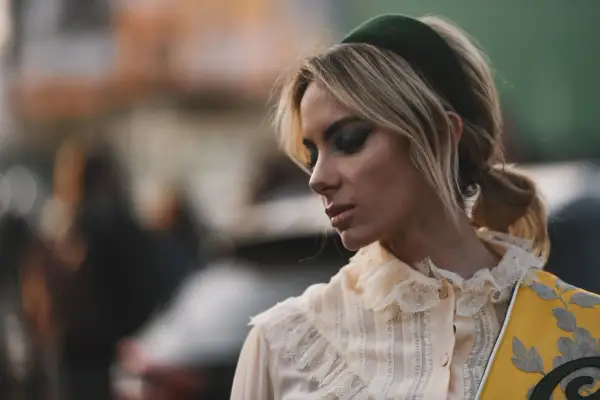 Blonde Frau mit auffälligem Make-up und einem grünen Haarband, das ihre Frisur betont.
