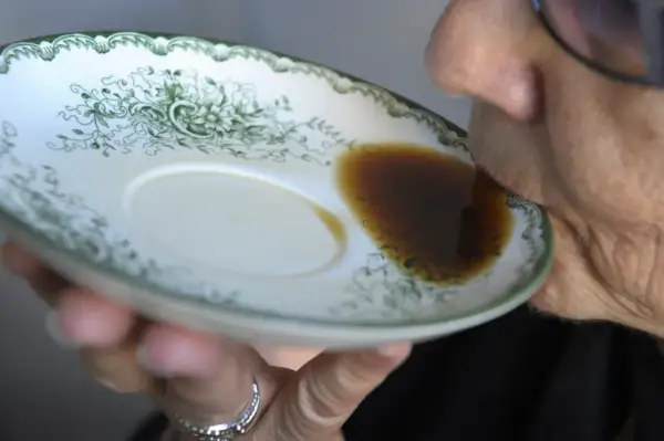 En person dricker gammalt kaffe direkt ur en tefat med grön dekor.