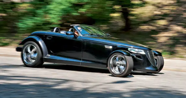 Czarny Plymouth Prowler z opuszczonym dachem pędzi po krętej drodze, otoczony rozmazaną zielenią drzew.