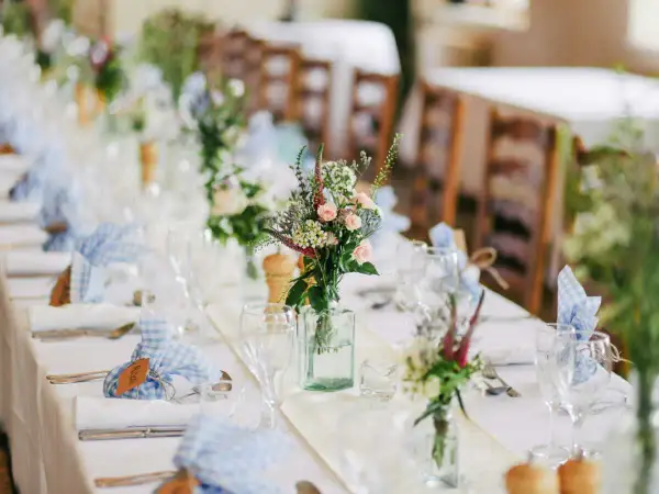 Décoration baptême champêtre à faire soi-même : table dressée avec nappes blanches, bouquets de fleurs sauvages, serviettes à carreaux bleus et bois.