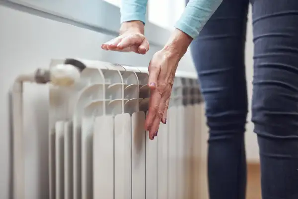 Ręce sprawdzają temperaturę grzejnika, zastanawiając się, dlaczego grzejnik jest zimny na dole.