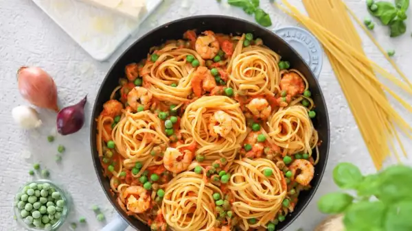 Linguine mit Garnelen und Erbsen in einer cremigen Tomatensauce, garniert mit frischem Basilikum.