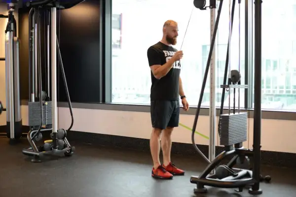 Mężczyzna wykonuje prostowanie ramion na wyciągu, ćwicząc triceps.