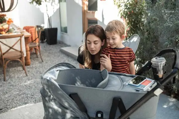 Mama i synek pochylają się nad gondolą spacerówki, jakby zastanawiali się, od kiedy spacerówka będzie im potrzebna.