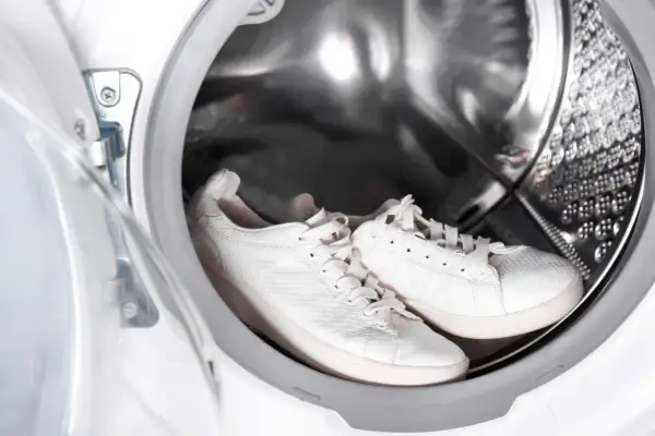 Weiße Sneaker warten im Inneren einer Waschmaschine auf ihren Einsatz.