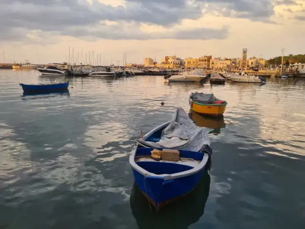 Barche nel porto al tramonto, con la città sullo sfondo. Un'atmosfera di pace e contemplazione, quasi un soffio di **santo spirito** sul mare calmo.