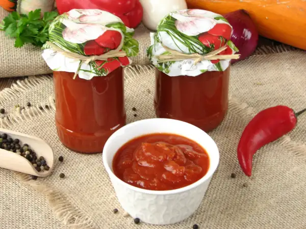 Domowy ketchup z cukinii w słoikach, miseczce i z papryczką chili.