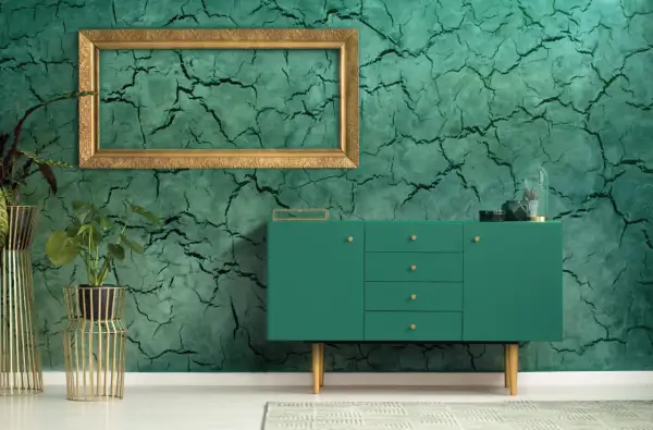 Parete con finitura in stucco materico verde intenso, incorniciata da un elegante mobile verde e piante in vasi dorati.
