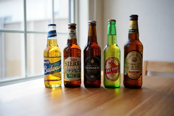 Cinque bottiglie di birra, tra cui Budweiser, Sierra Nevada e Guinness, pronte per essere raffreddate. La temperatura birra in frigo è ideale per gustarle al meglio.