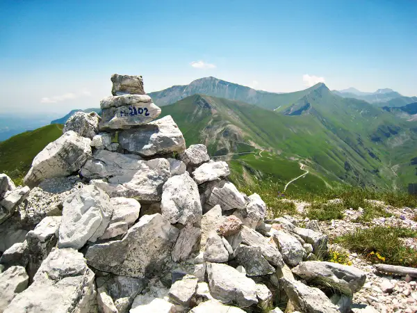 Cairn con M. 2102, simbolo di un'avventura di trekking nei Monti Sibillini. Panoramica mozzafiato sulle verdi valli e sentieri tortuosi.