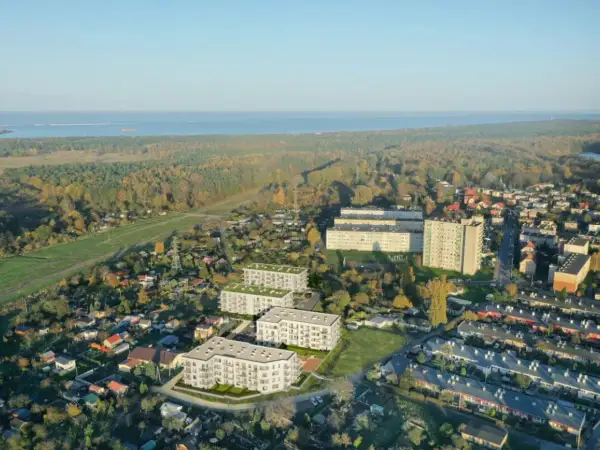 Nowoczesne bloki mieszkalne wyrastają pośród zieleni i domów jednorodzinnych, tworząc nowe młode stogi w krajobrazie. W tle morze i jesienny las.