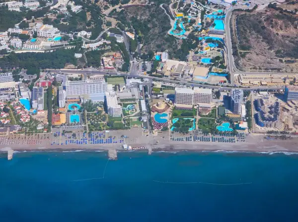 Vy från ovan över ett stort vattenland och hotellkomplex vid Rhodos kust. Solstolar och parasoller kantar stranden.