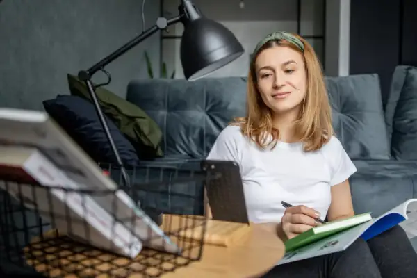 Kobieta uczy się w domu, notując w zeszycie. To idealny moment, by zgłębiać wiedzę, gdy czujemy się wypoczęci i skupieni.