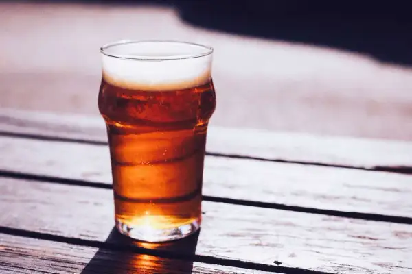 Un bicchiere di caña birra con schiuma bianca, illuminato dal sole, su un tavolo di legno all'aperto.