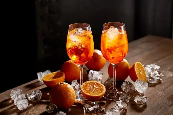 Dwa kieliszki Aperol Spritz, pomarańcze i lód na drewnianym stole. Aperol co to? Orzeźwiający drink na lato.