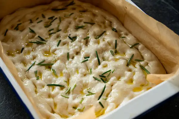 Luftiger focaccia teig mit Rosmarin und Olivenöl in einer Backform, bereit zum Backen.