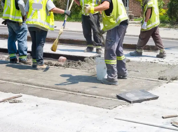 Prace interwencyjne: robotnicy w kamizelkach odblaskowych wylewają beton na torowisko.
