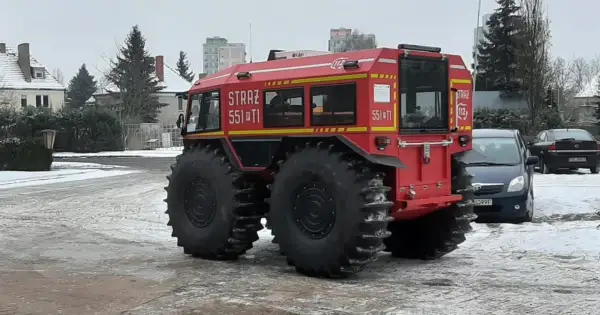 Czerwone auto straż pożarna z wielkimi oponami, gotowe do akcji w trudnym terenie.