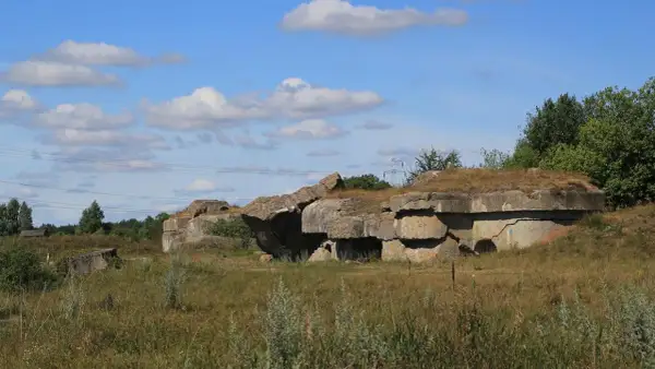 Ruiny fortu Osowiec, betonowe bunkry porośnięte trawą, na tle błękitnego nieba z chmurami.