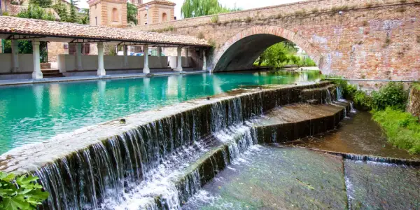 Cascata d'acqua cristallina sotto un antico ponte in mattoni, un angolo di pace tra i borghi medievali umbri.