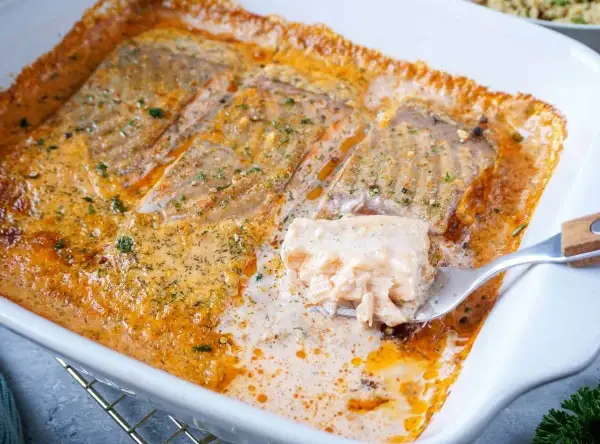 Saftiges Lachsfilet in cremiger Sahnesauce, ein köstliches Lachs Sahne Gratin, wird mit einer Gabel herausgehoben.