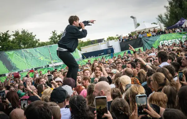 Sänger auf dem Dach eines Containers beim Green Juice Festival, der ins jubelnde Publikum zeigt. Viele Handys halten die Momente fest.