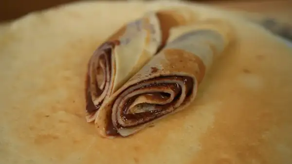 Zwei gerollte low carb pfannkuchen mit Schokoladencreme, auf einem größeren Pfannkuchen liegend.
