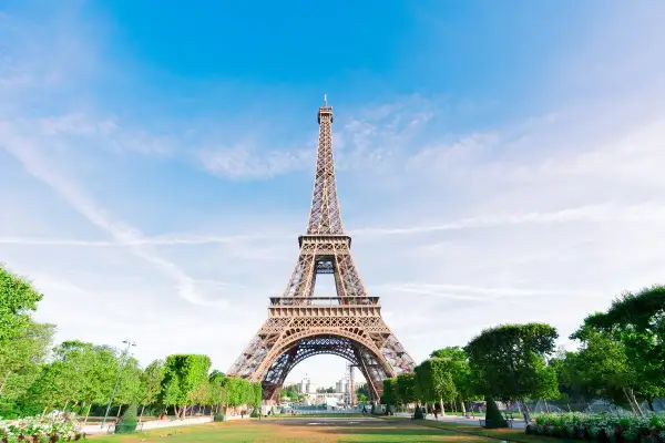 La icónica Torre Eiffel, un ejemplo del estilo arquitectónico de la época, se alza majestuosa bajo un cielo azul con nubes dispersas.
