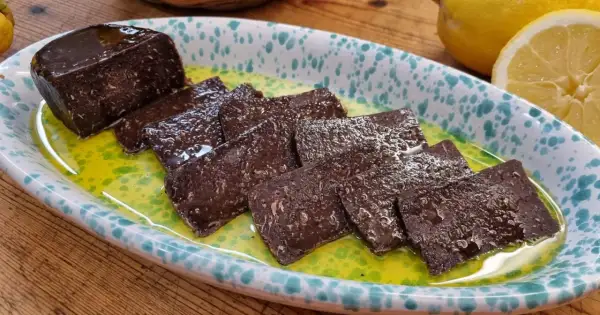 Fette di salame di tonno scuro, lucido e saporito, servite in una ciotola con olio verde e limone.