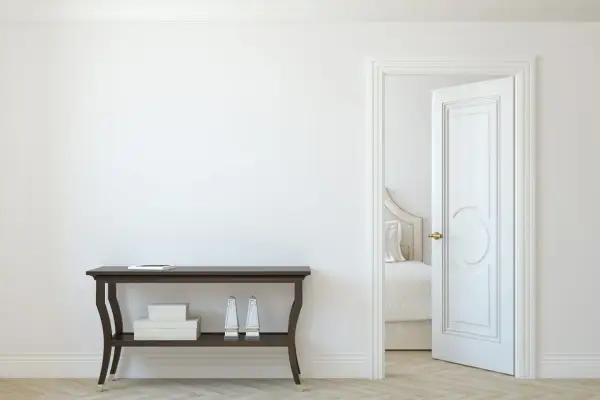 Un corridoio con un tavolino scuro e una porta aperta che rivela una stanza da letto. La porta interna è dipinta di bianco, con un design classico.