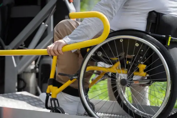 Persona in sedia a rotelle si aggrappa a un corrimano giallo, suggerendo un noleggio auto con legge 104 per maggiore accessibilità.