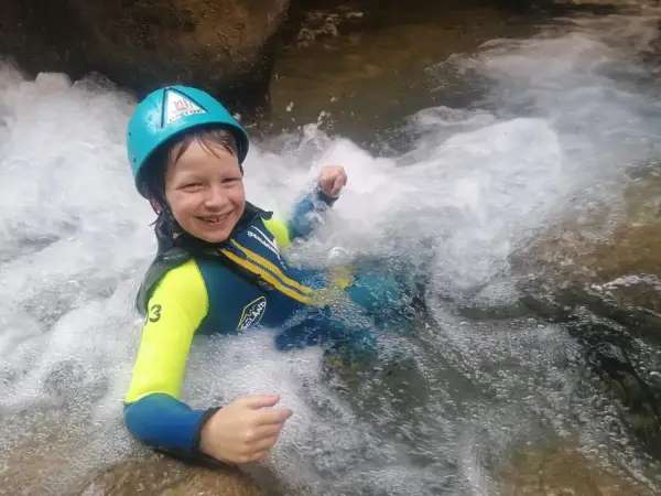 Niño sonriente con casco y traje de neopreno disfrutando del barranquismo en la Sierra de Guara. ¡Una aventura de senderismo acuático inolvidable!