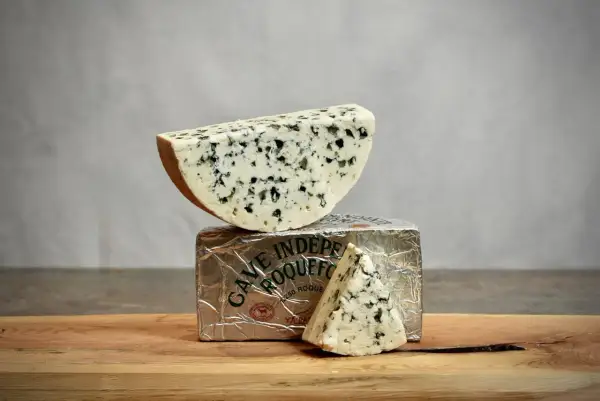 Un morceau de roquefort est posé sur son emballage argenté, avec une autre part en triangle à côté.