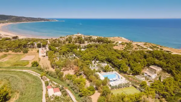 Vista aerea della baia della Tufara con mare azzurro, spiaggia dorata, pineta lussureggiante, piscina e campo da tennis.