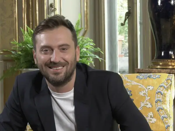 Un uomo sorride, con un blazer scuro e una maglietta bianca. I testi di Cesare Cremonini dicono di me che sono felice.