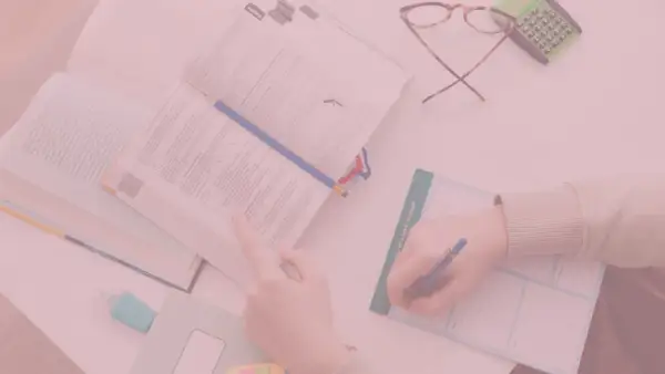 Otwarta książka, ręka pisząca w notatniku, okulary i kalkulator.