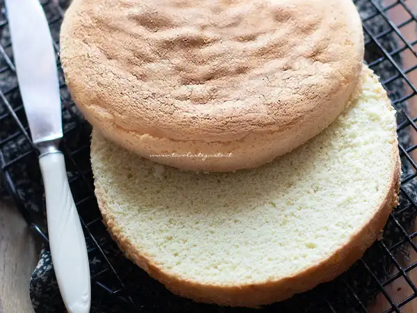 Due dischi di pan di spagna senza glutine, uno sopra l'altro, su una griglia. Un coltello è visibile a sinistra.