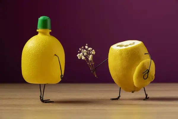 Un limone con gambe di filo offre un mazzolino di fiori a un altro limone con tappo verde. Un divertente shooting still life.