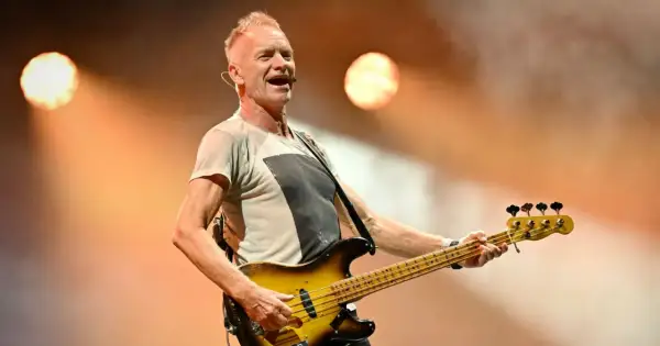 Sting, lider zespołu The Police, gra na gitarze basowej na scenie, oświetlony ciepłym światłem.