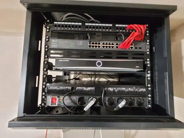 W szafie sieciowej znajduje się router, switch TP-Link, rejestrator Hikvision i listwa zasilająca.