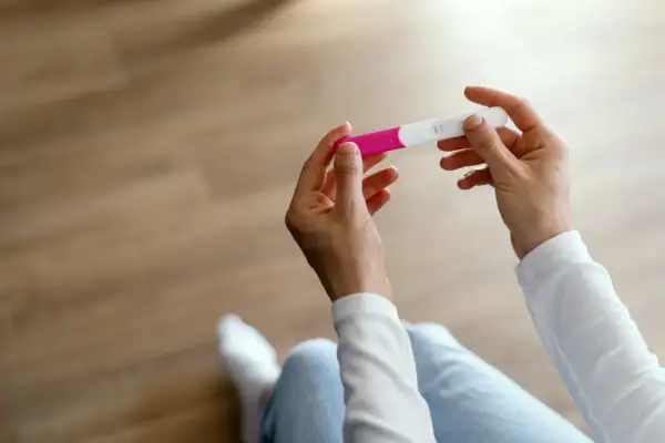 Dłonie trzymające test ciążowy. Wynik wskazuje na wczesny etap, być może 1 tydzień ciąży.