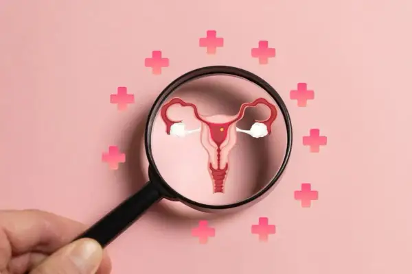 Powiększona macica i jajniki pod lupą, otoczone różowymi krzyżykami. Ilustracja symbolizuje diagnostykę i leczenie PCOS objawów.
