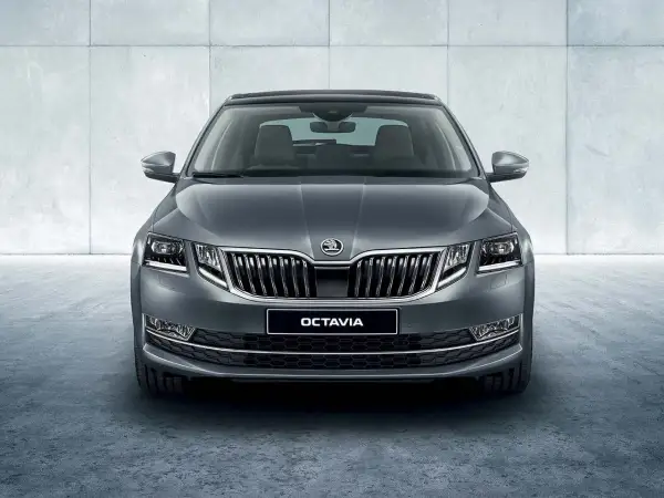 Szary Skoda Octavia sedan z chromowanym grillem i światłami LED, prezentujący się elegancko na tle betonowej ściany.