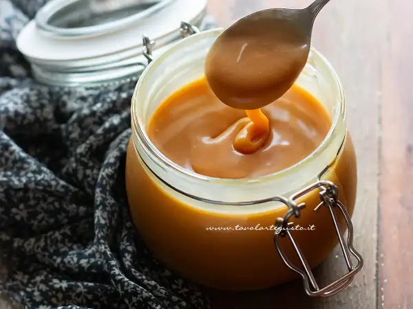 Un cucchiaio raccoglie un denso caramello salato da un barattolo di vetro.