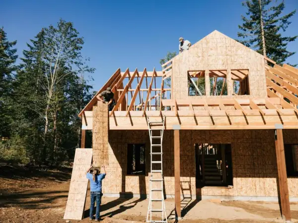 Construcción de una casa de madera, con obreros colocando tableros. El proceso de saber cuanto cuesta hacer una casa es complejo.
