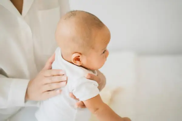 Delikatne dłonie trzymają noworodka w białej koszulce. Mama szuka sposobów, co na czkawkę u noworodka, by ukoić maluszka.