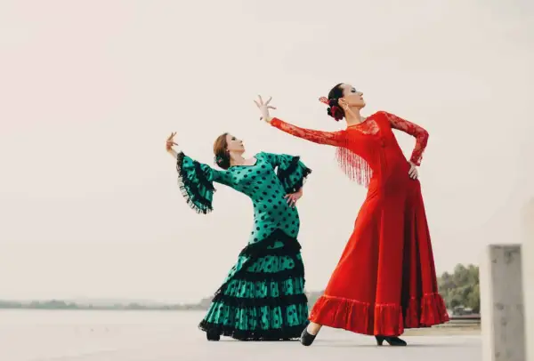 Dos mujeres bailan flamenco. Una con vestido verde de lunares, la otra con rojo. Inspiración para palos del flamenco para niños.