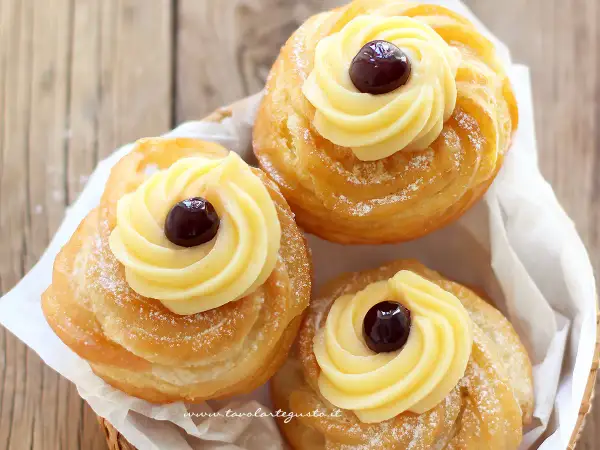 Tre zeppole fritte napoletane, dorate e spolverate di zucchero a velo, con crema pasticcera e una ciliegina.