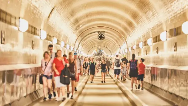 Menschen gehen durch den hell erleuchteten, gewölbten Gang des alten Elbtunnels.